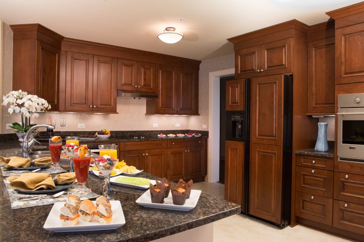 A modern kitchen with wooden cabinets, dark countertops, and a variety of food items displayed.