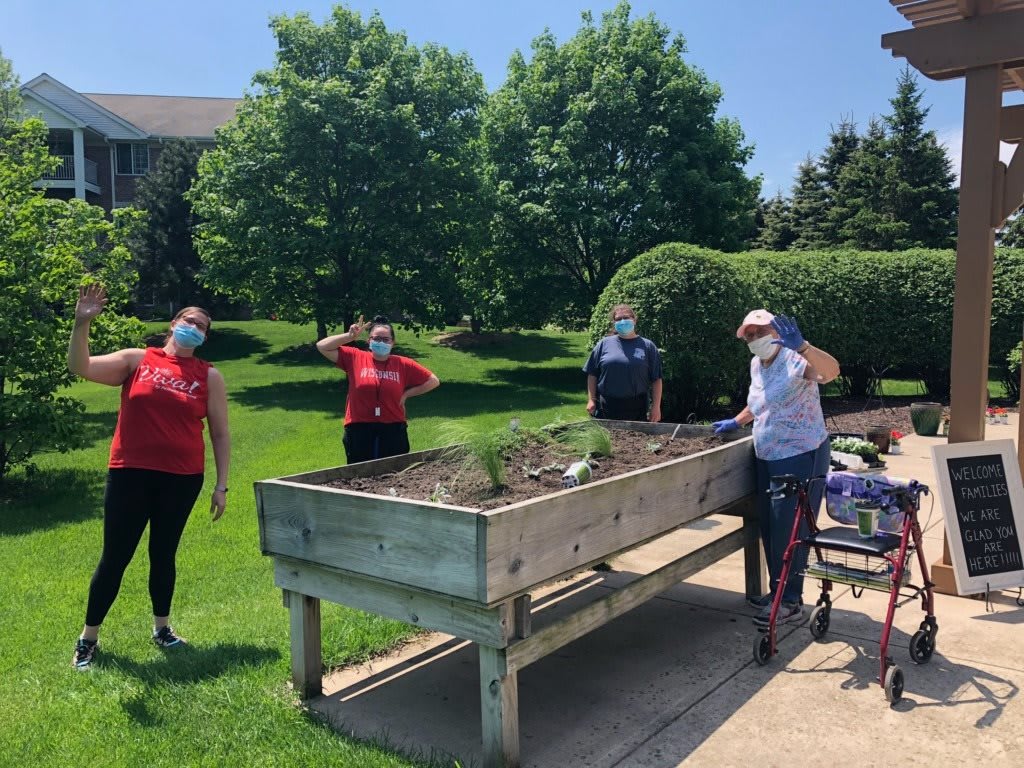 A group of people wearing masks are gardening together outdoors on a sunny day.