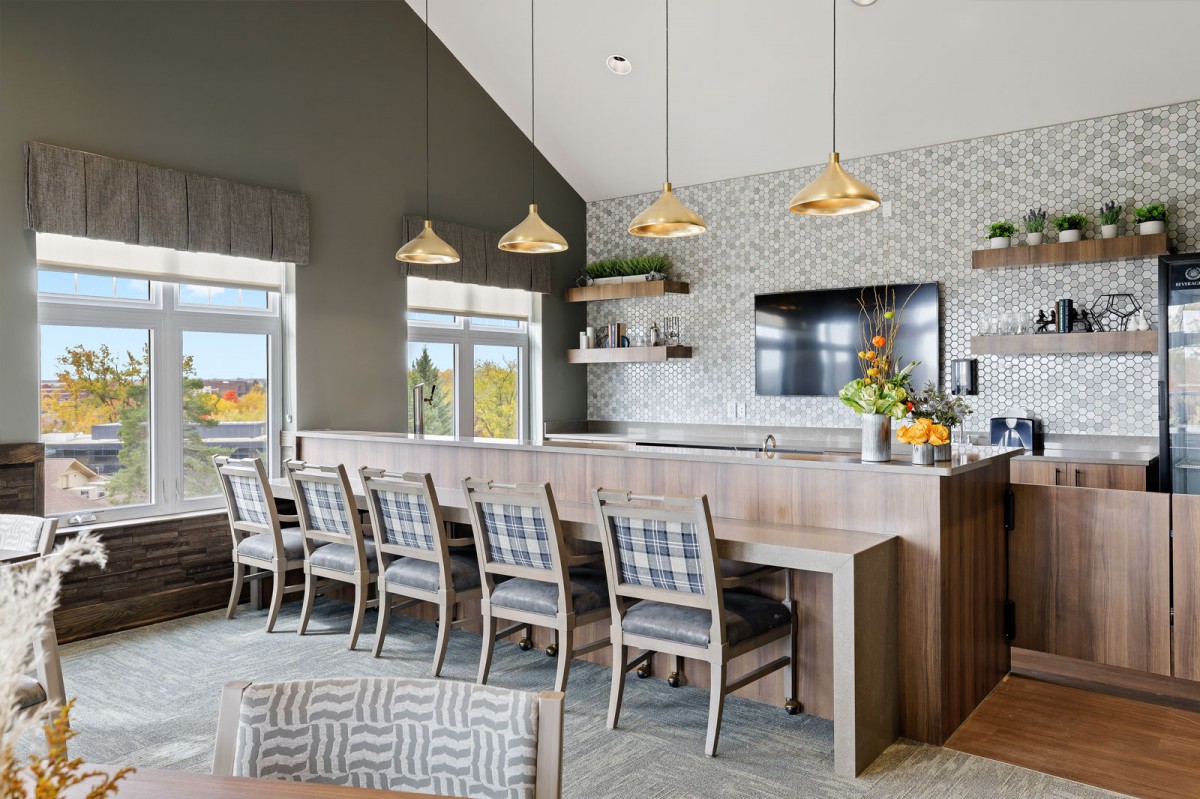 A modern dining area with a long table, plaid chairs, and stylish pendant lights in a contemporary setting.
