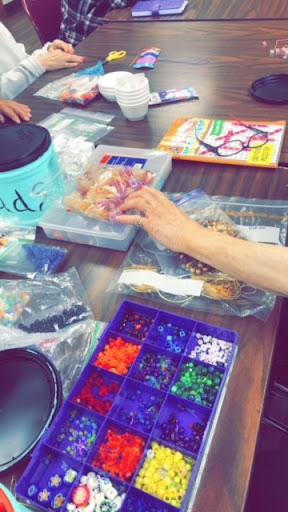 A table filled with various craft supplies, showcasing vibrant beads and hands engaged in a creative project.