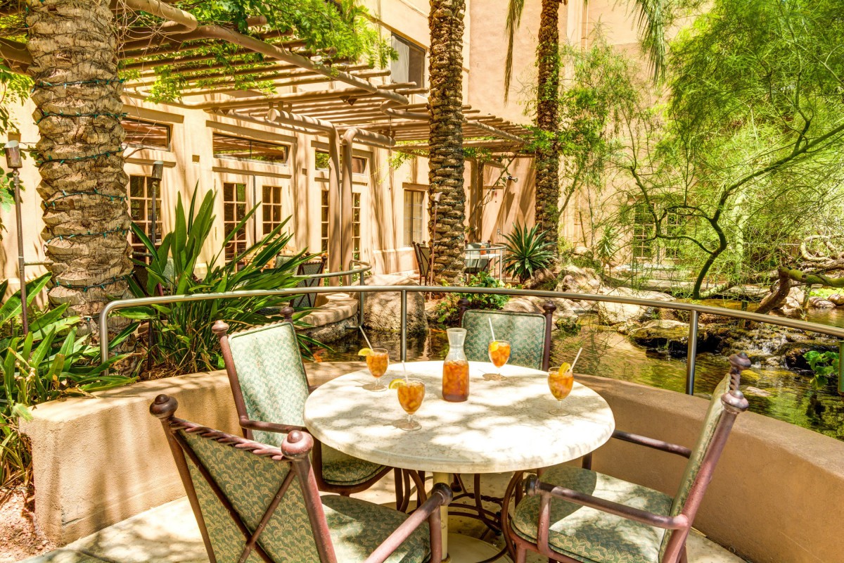 A sunny patio with a round table and chairs, surrounded by lush tropical plants.