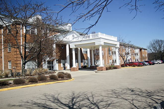 A large building with a covered entrance supported by white columns, surrounded by trees.