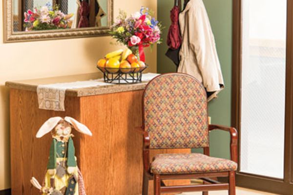 A cozy interior with a chair, a fruit basket, and flowers next to a mirror.