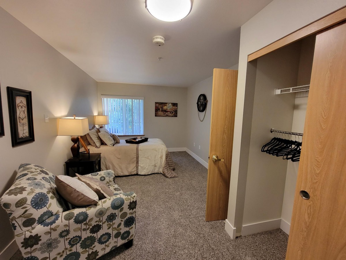 A cozy bedroom with a bed, sofa, lamps, and a small closet.