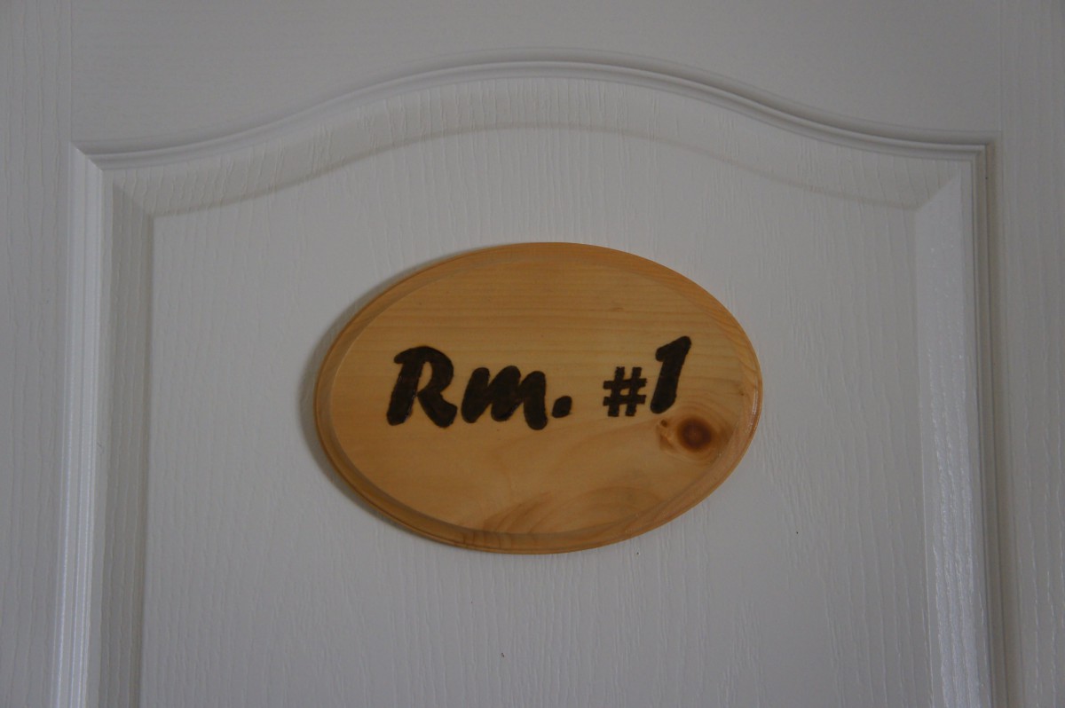 An oval wooden sign on a door indicating 'Rm. #1'.