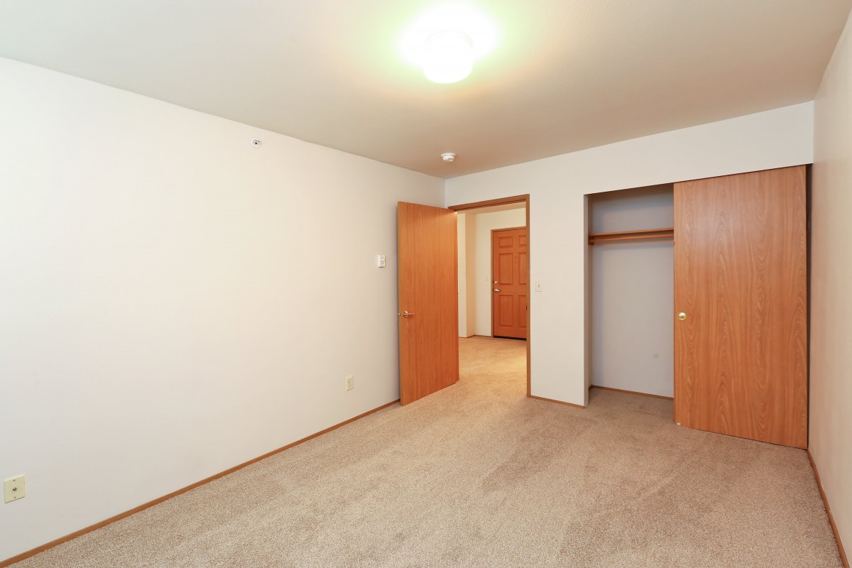 An empty room with a carpeted floor, a closet, and wooden doors.