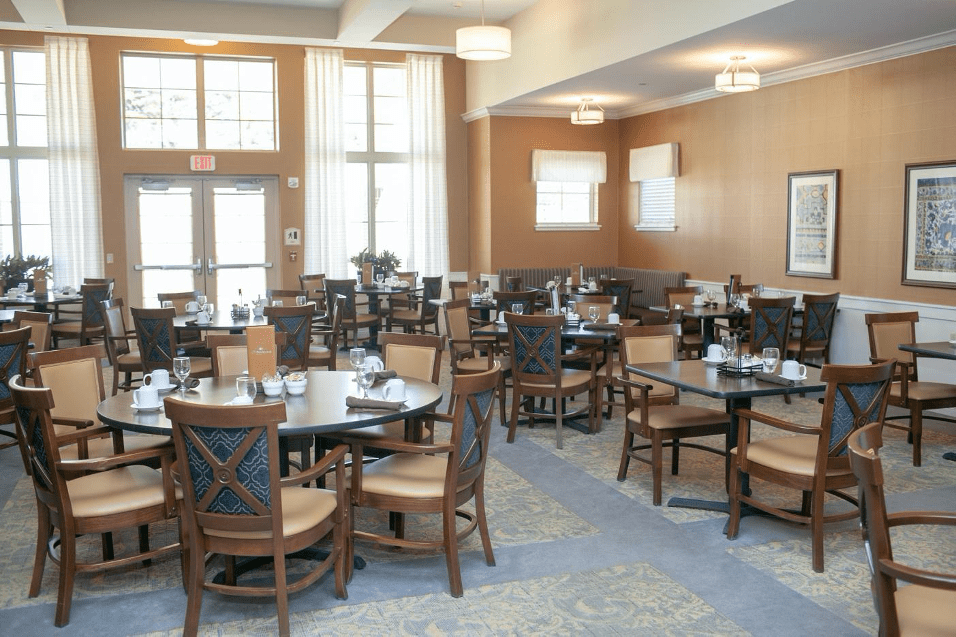 A modern dining room with neatly arranged tables and chairs, featuring large windows and neutral tones.