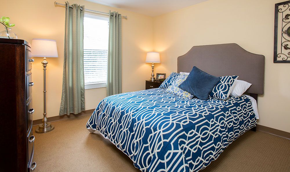 A cozy bedroom with a patterned bedspread, soft lighting from a lamp, and a window with curtains.