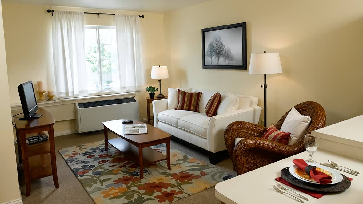 A cozy living room with a sofa, armchair, and coffee table, complemented by a carpet and decorative artwork.