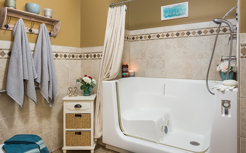 A cozy bathroom featuring a walk-in tub, adorned with elegant tiles and soft lighting from a lit candle.
