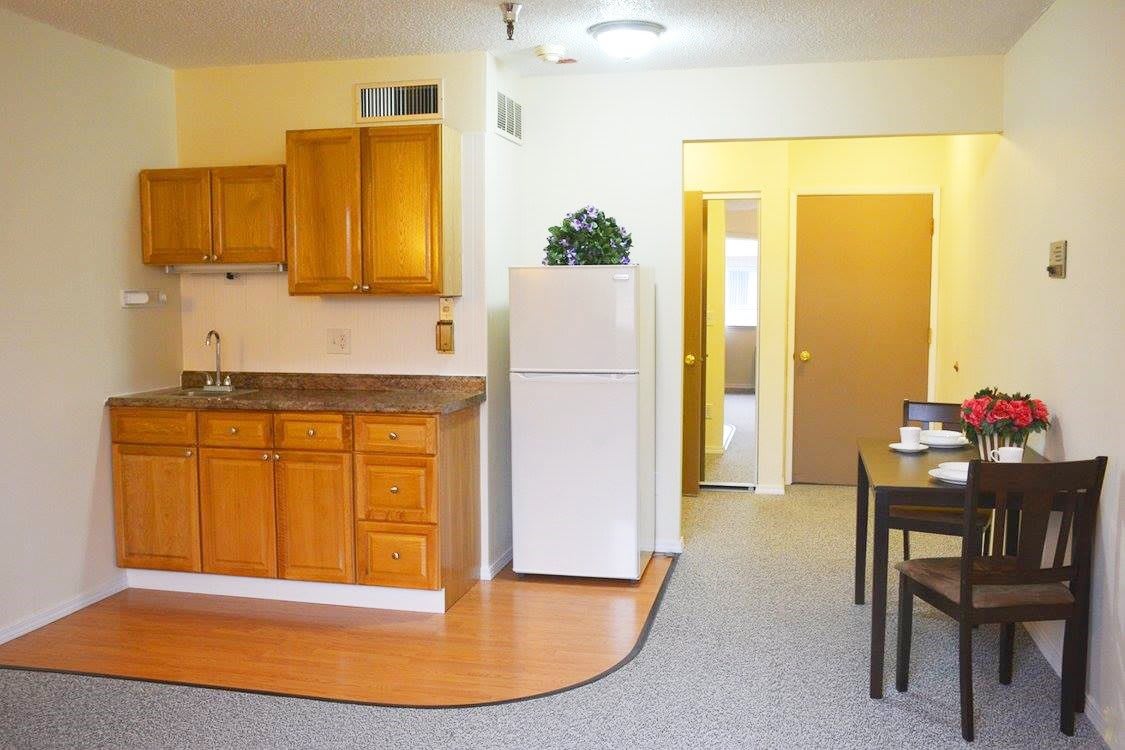 An interior view of a small apartment kitchen with wooden cabinets and a dining area.