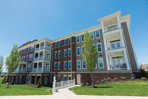 A modern apartment building featuring balconies and a well-maintained landscape under a clear blue sky.