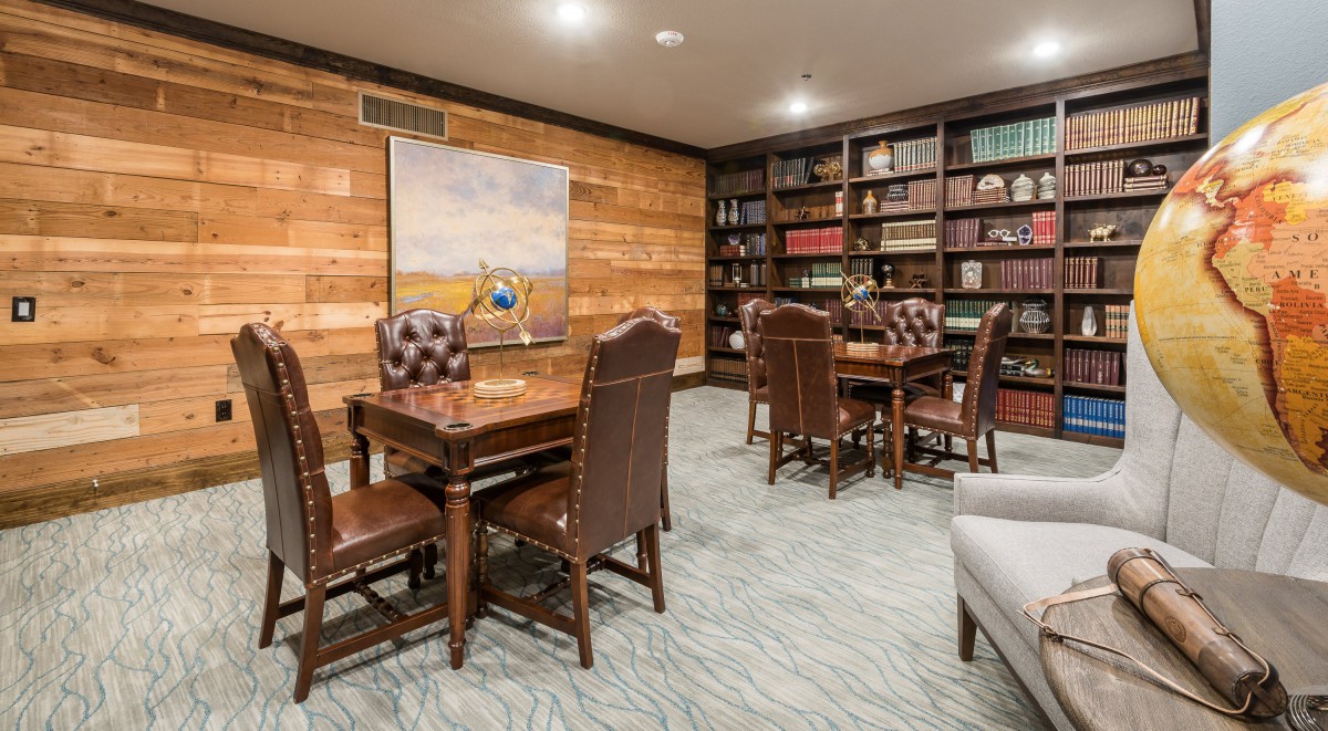A cozy reading room with leather chairs, wooden tables, and bookshelves filled with books.