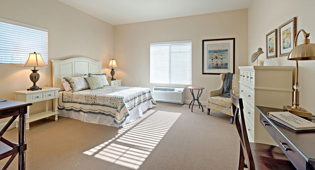 A cozy bedroom with a neatly made bed, armchair, and soft natural lighting from the window.