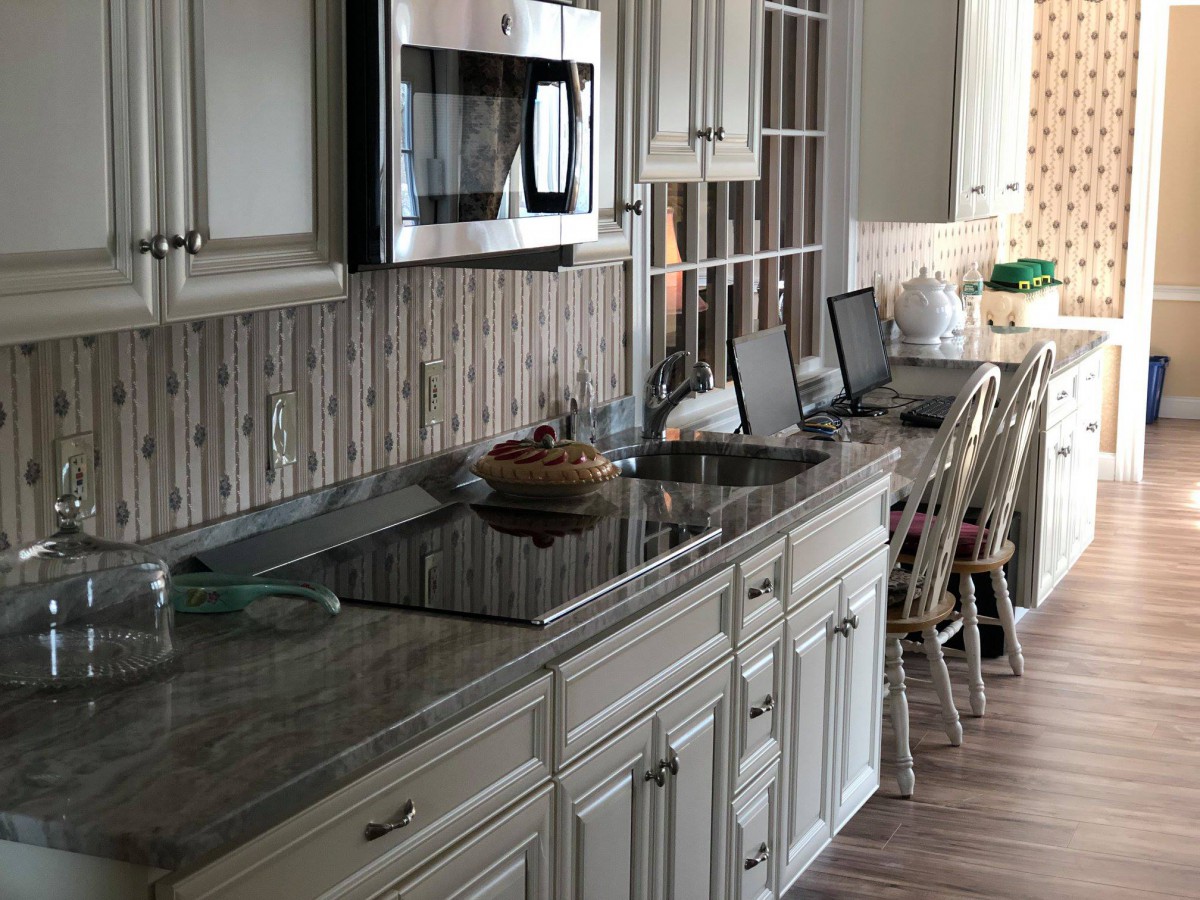 A modern kitchen with sleek countertops, featuring a microwave, laptops on the counter, and a cupcake stand.