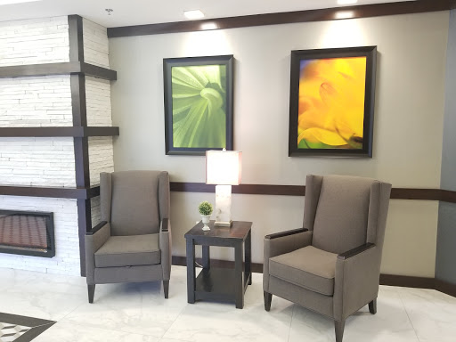 A cozy seating area in a modern interior space featuring two armchairs, a small table with a lamp, and decorative wall art.