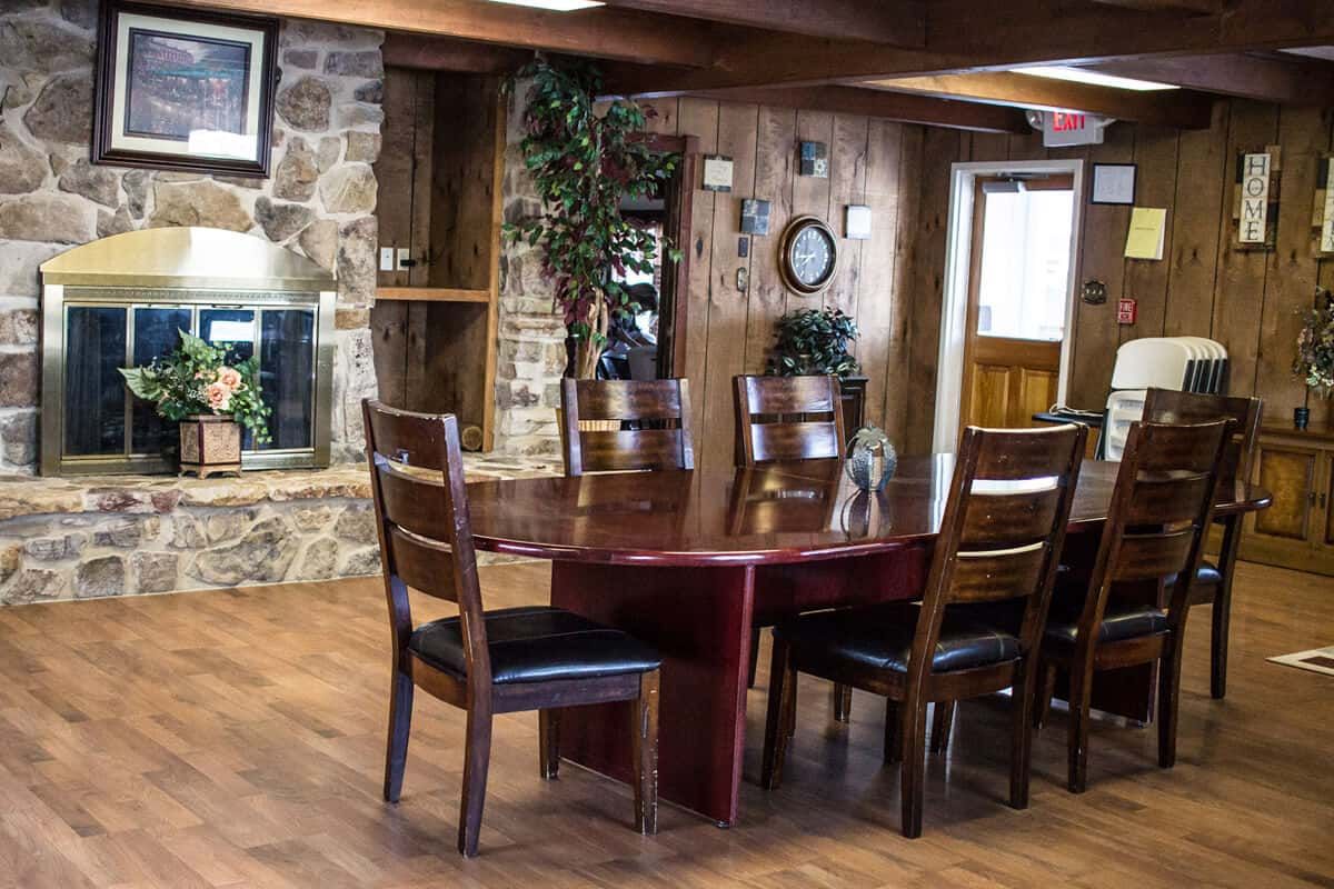 A cozy dining area with a wooden table, chairs, and a stone fireplace, featuring rustic decor and indoor plants.