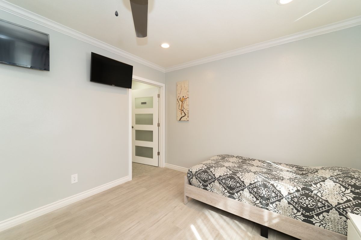 A modern minimalist bedroom with a television, elegant bedding, and wooden flooring.