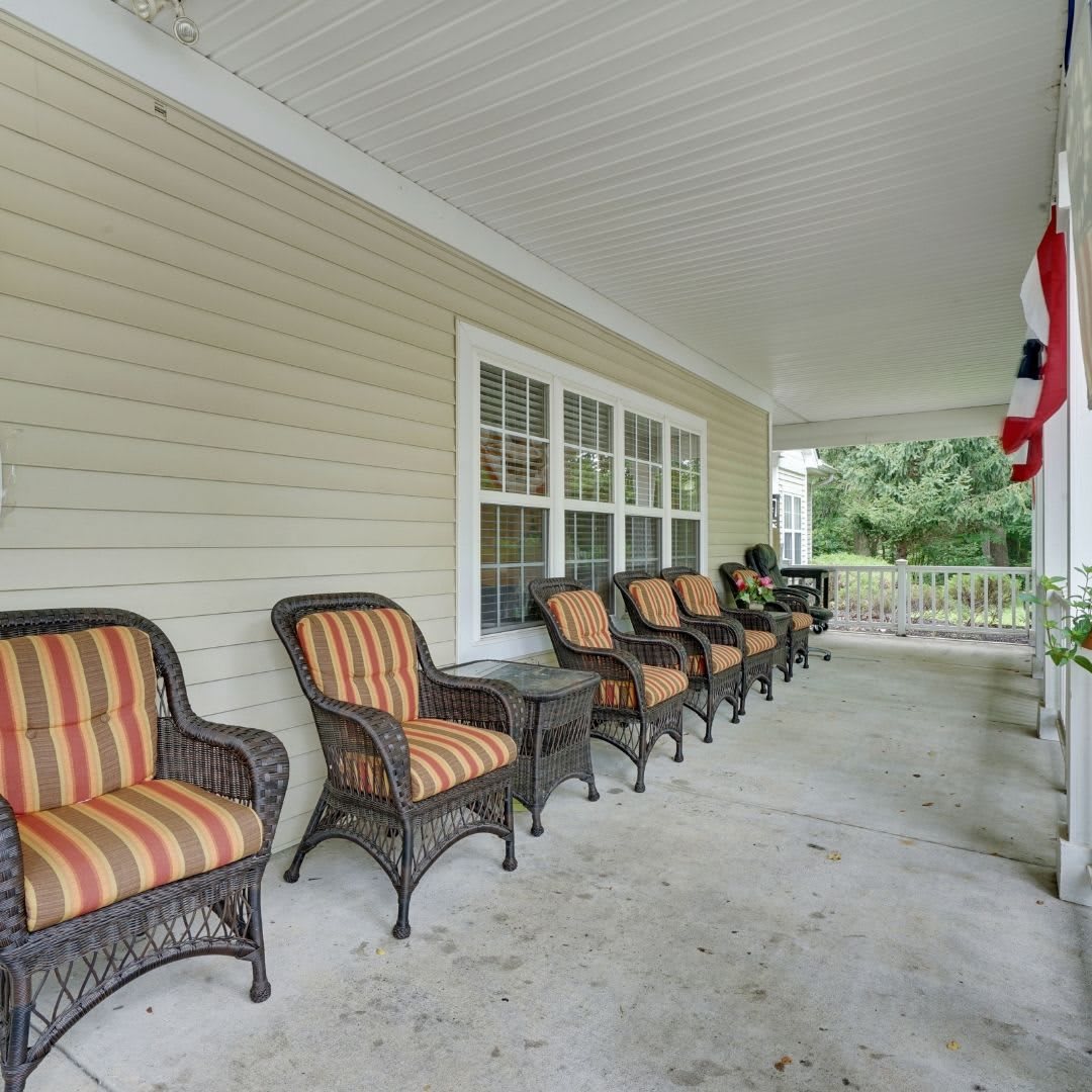 A covered porch with a row of wicker chairs featuring striped cushions.