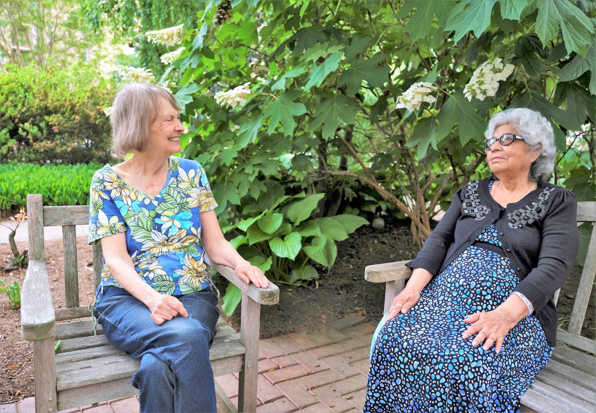 Two women sitting on benches and having a conversation in a garden.