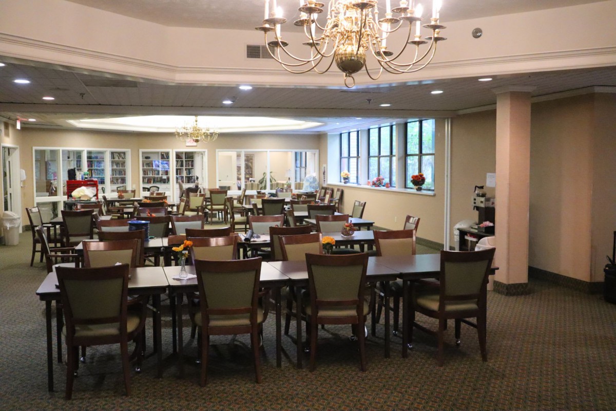 An elegant dining area with multiple tables and chairs, illuminated by chandeliers.