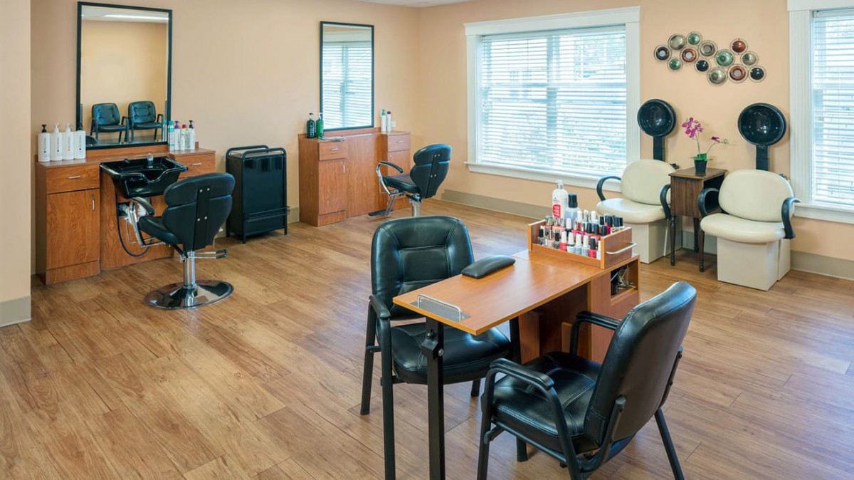 A bright and welcoming hair and beauty salon interior with multiple chairs, a nail station, and large windows.