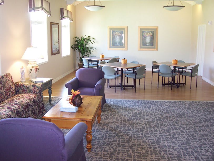 A cozy seating area with purple chairs and wooden tables, decorated with framed art and plants.
