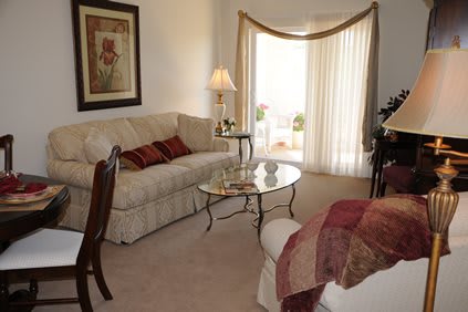 A cozy and elegantly decorated living room with a sofa, glass coffee table, lamp, and wall art.
