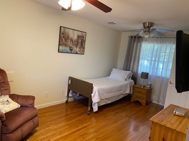 A cozy bedroom featuring a single bed with white linens, a wooden nightstand, and a ceiling fan.