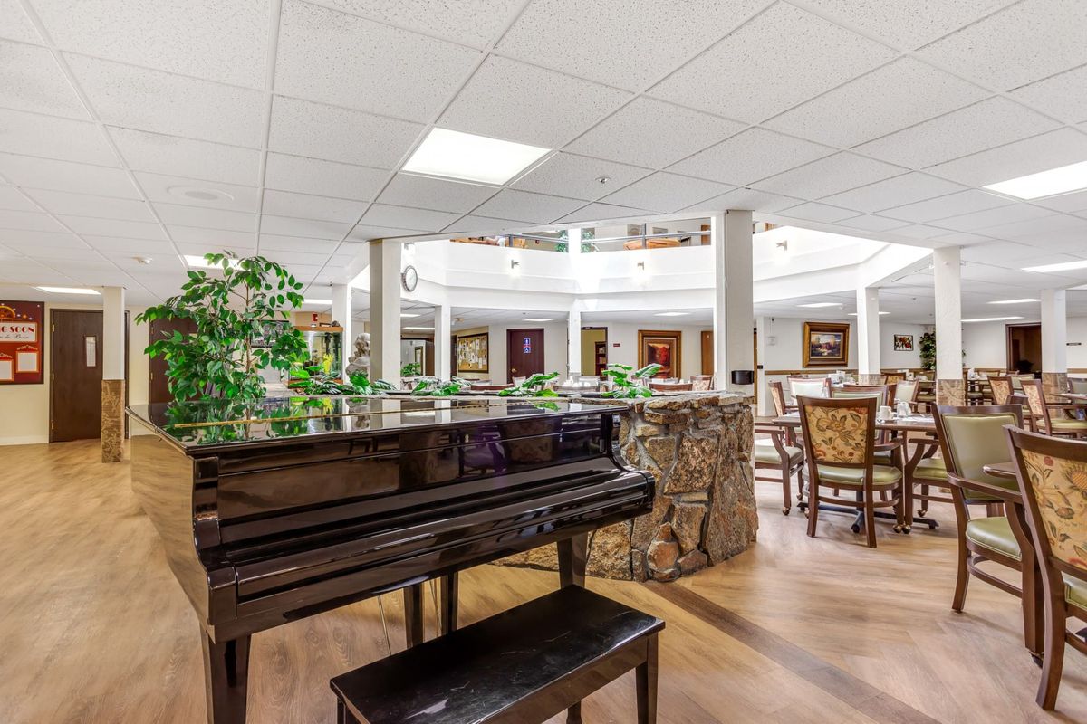 A spacious lobby area with a piano, surrounded by chairs, tables, and greenery.
