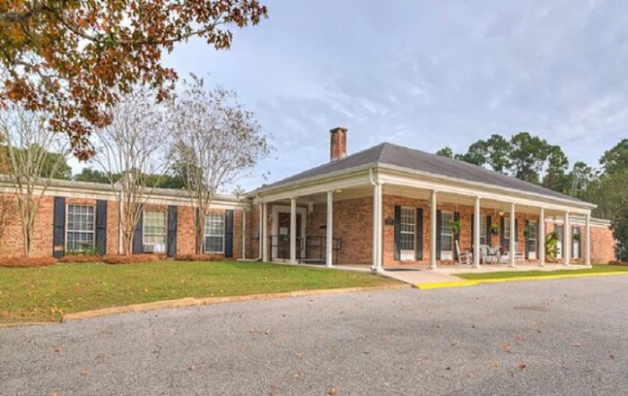 A brick house with a covered porch and a driveway, surrounded by trees.