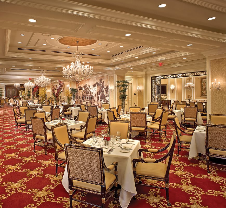 A luxurious restaurant dining room with elegant decor, featuring chandeliers and a richly carpeted floor.