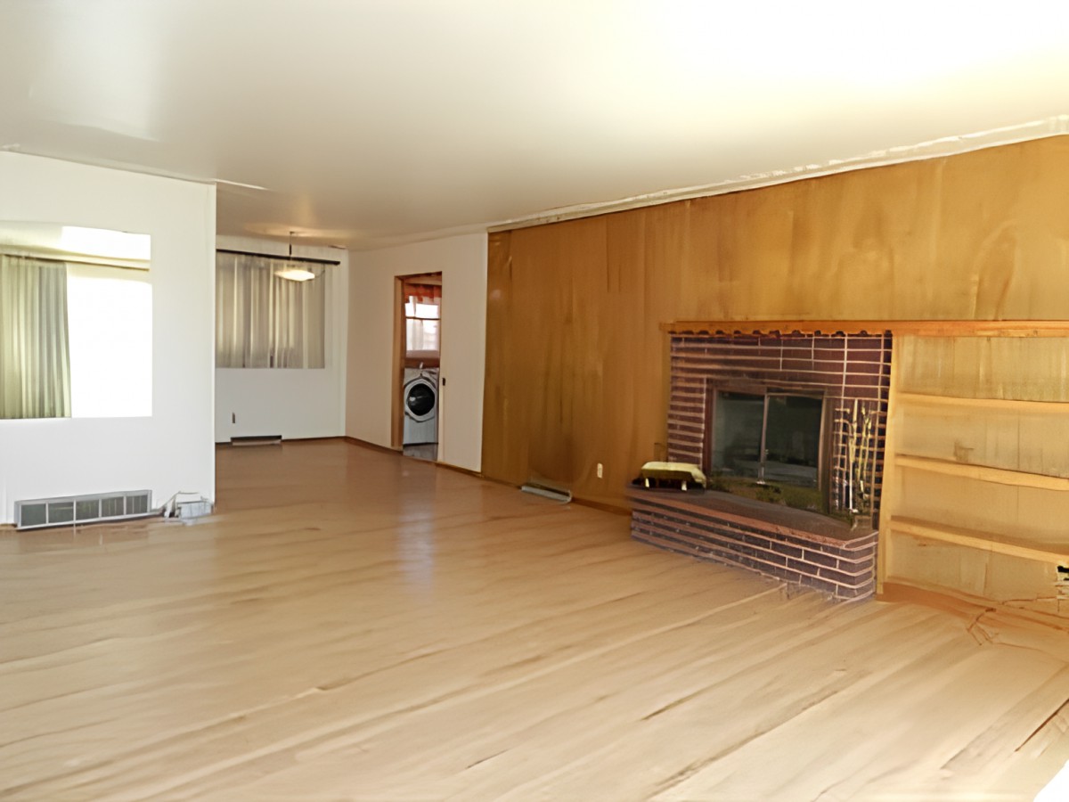A spacious living room featuring hardwood floors and a brick fireplace with wood paneling.