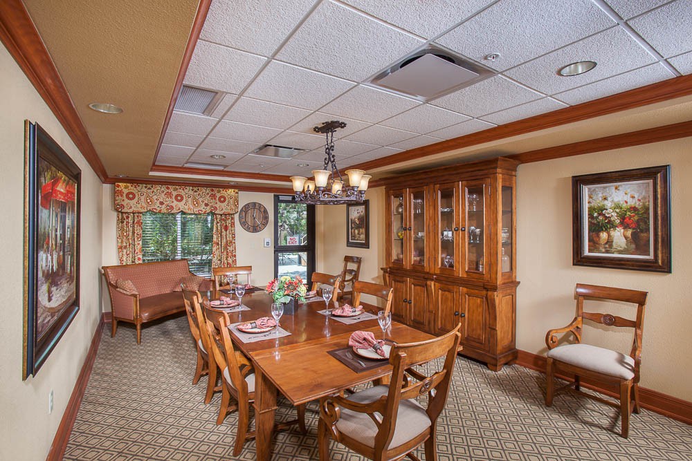 A well-furnished dining room with a long wooden table, chairs, and a china cabinet, adorned with a chandelier and large windows.
