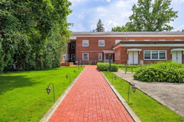 A brick house with a red pathway leading through a green lawn under a sunny sky.
