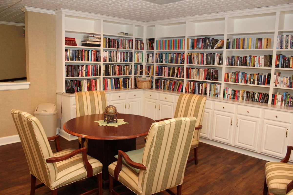 A cozy study room with bookshelves full of books, a round table, and comfortable chairs.