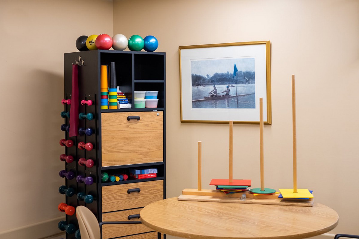 A therapy room featuring exercise equipment such as colorful balls, weights, and rehabilitation tools on shelves.