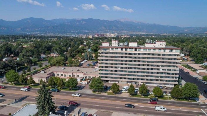 A city landscape featuring a large building with mountains in the background and a road lined with trees.