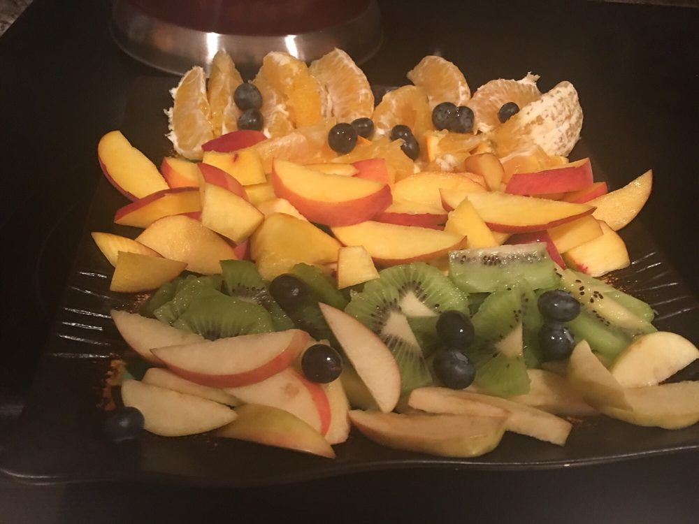 A colorful fruit platter featuring slices of oranges, peaches, kiwi, apples, and a scattering of blueberries.