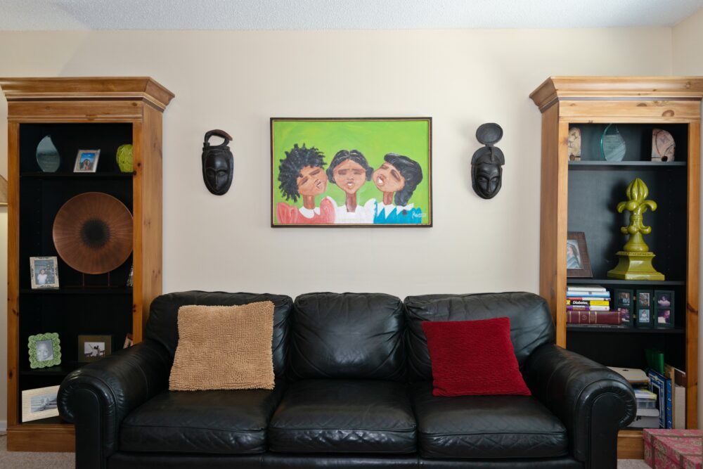 A cozy living room with a black leather sofa adorned with colorful pillows, surrounded by unique art and decor.