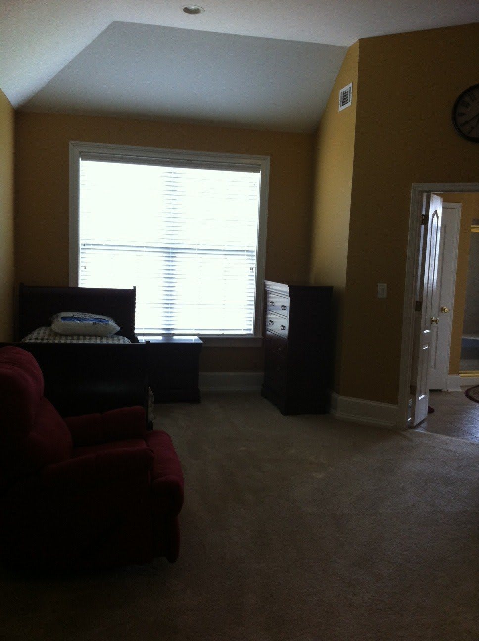 A well-lit room with furniture, including a bed, dresser, and armchair.