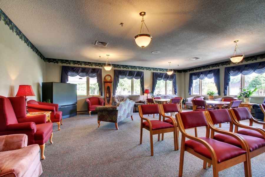 A cozy living room with multiple seating areas, featuring red chairs and large windows.