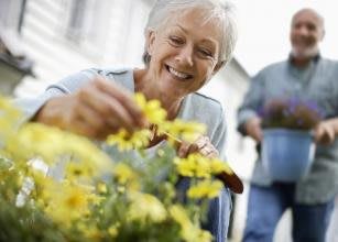 An elderly woman happily tending to flowers in her garden.