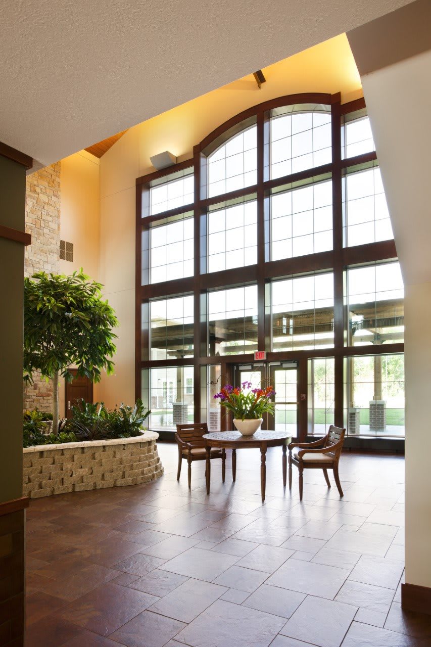 A spacious lobby with large windows, a seating area, and indoor plants, showcasing modern interior design.