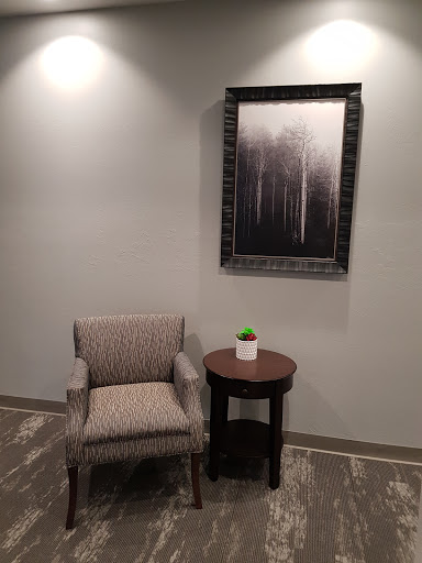 A cozy corner featuring a patterned chair and a small table with a plant, complemented by abstract artwork on the wall.