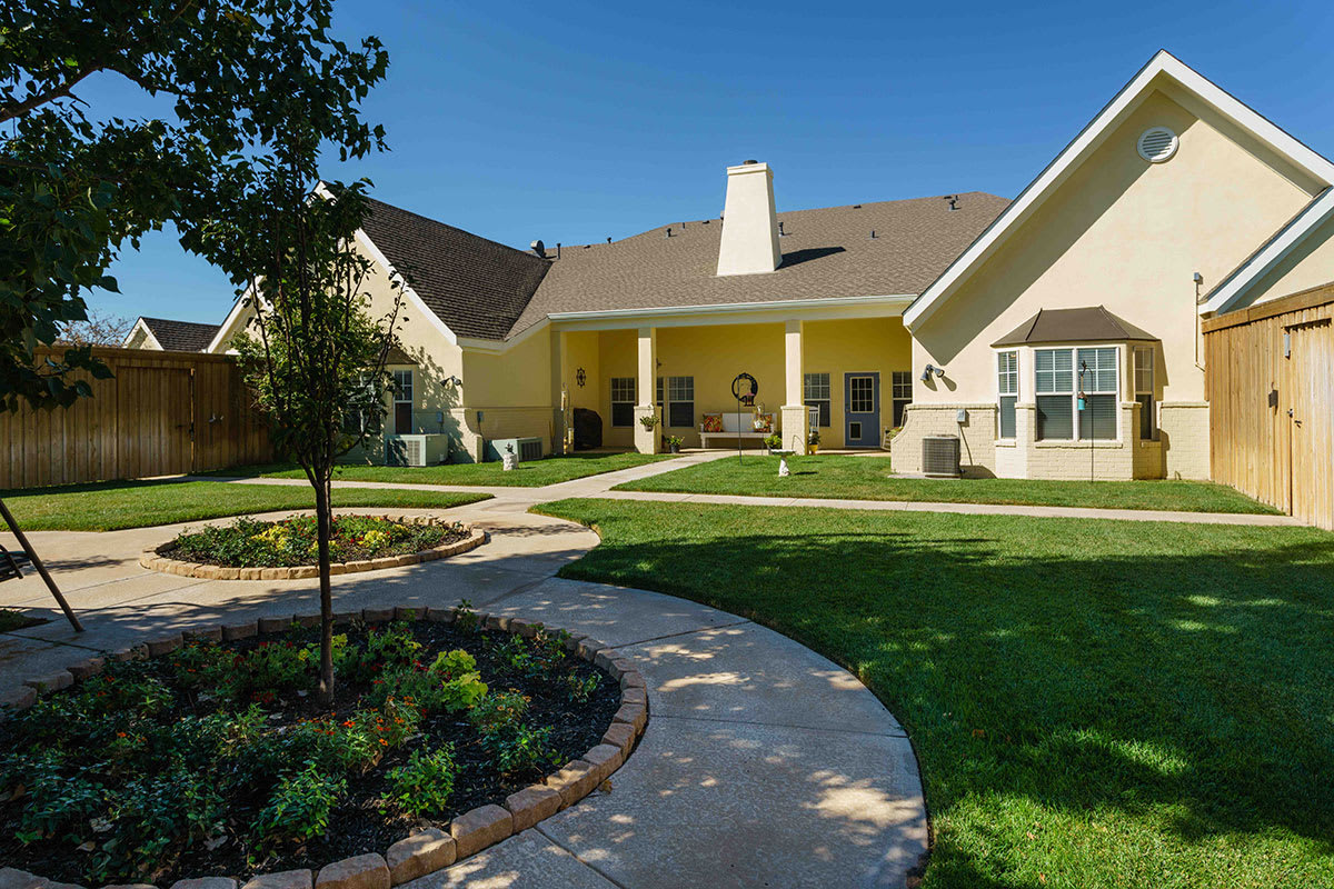 A well-maintained backyard with a garden, lawn, and a curving pathway leading to the house.