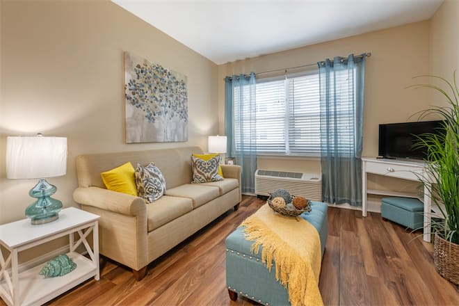 A cozy living room with a beige sofa, colorful pillows, and a stylish coffee table, illuminated by natural light streaming through sheer curtains.