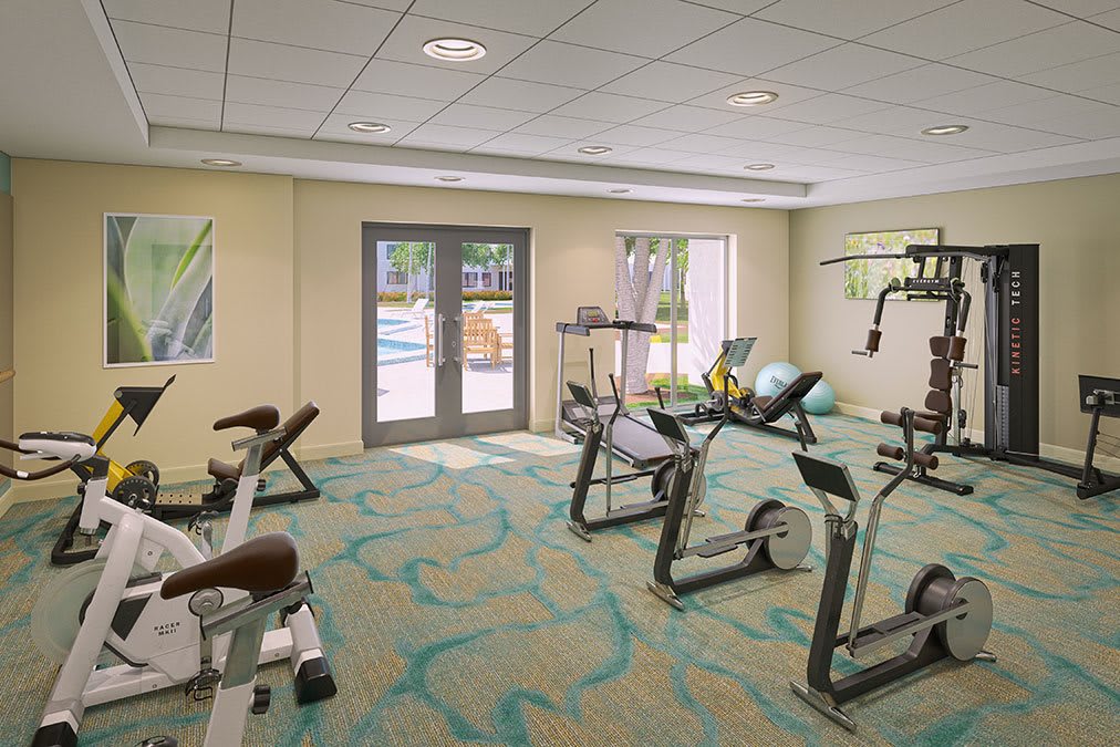 A well-lit gym with various exercise equipment and a view of an outdoor pool.