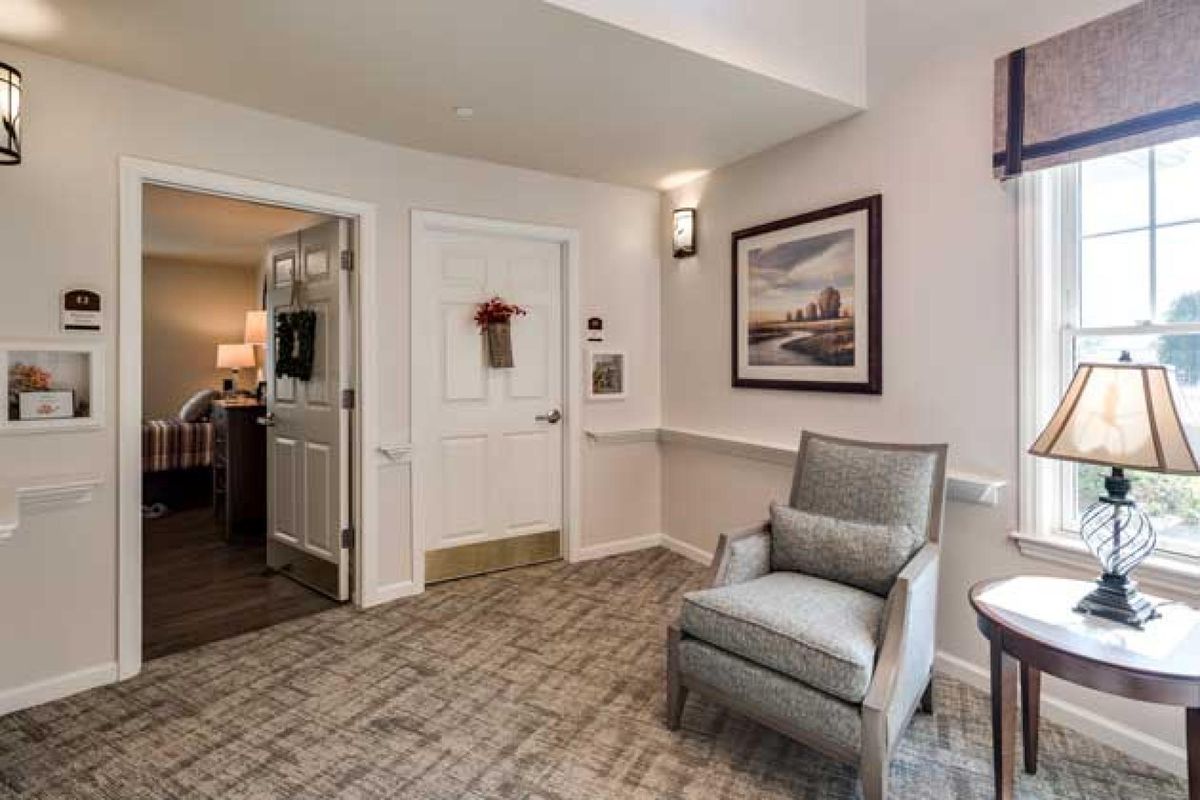 A cozy interior space with a chair, artwork on the wall, and a door leading to another room.