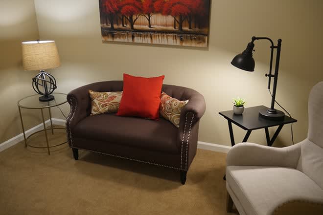 A cozy living room with a brown sofa, vibrant red cushion, and artistic wall decor.